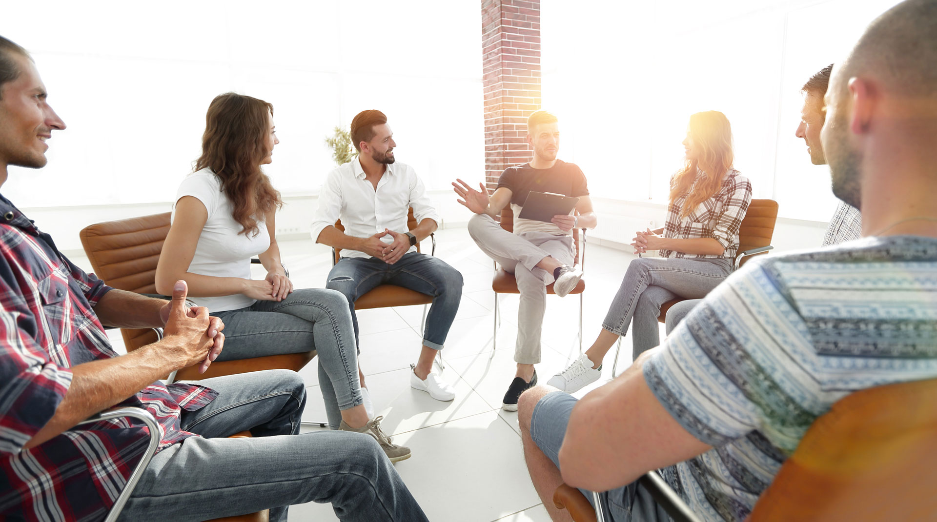 Group of people engaged in PTSD treatment session with a therapist in a bright room Group of people engaged in PTSD treatment session with a licensed mental health professional