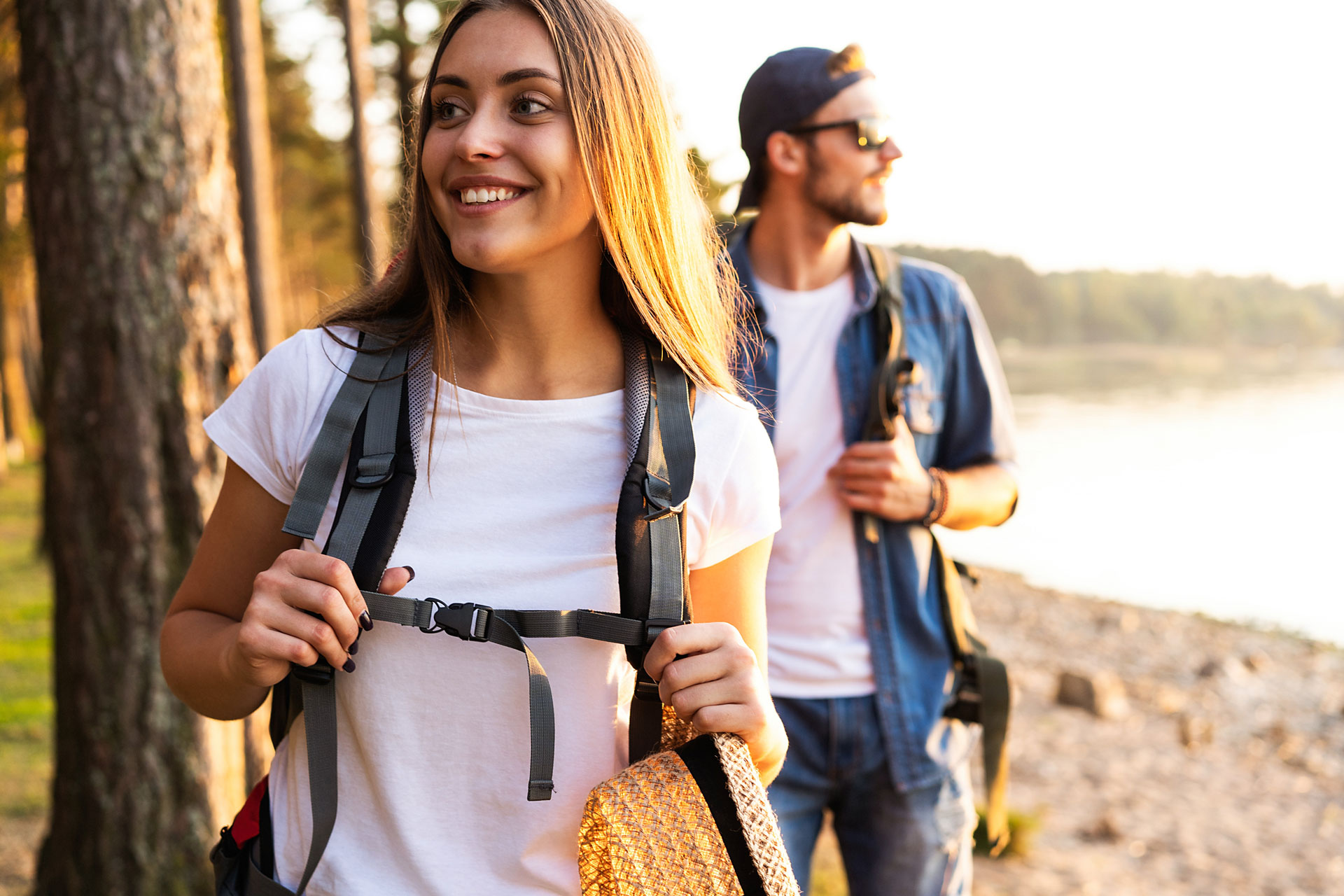 Smiling couple with backpacks enjoying a hike, possibly part of an Outpatient Programs activity Happy couple hiking by a lake at sunset, promoting the benefits of outdoor activities during heroin addiction treatment