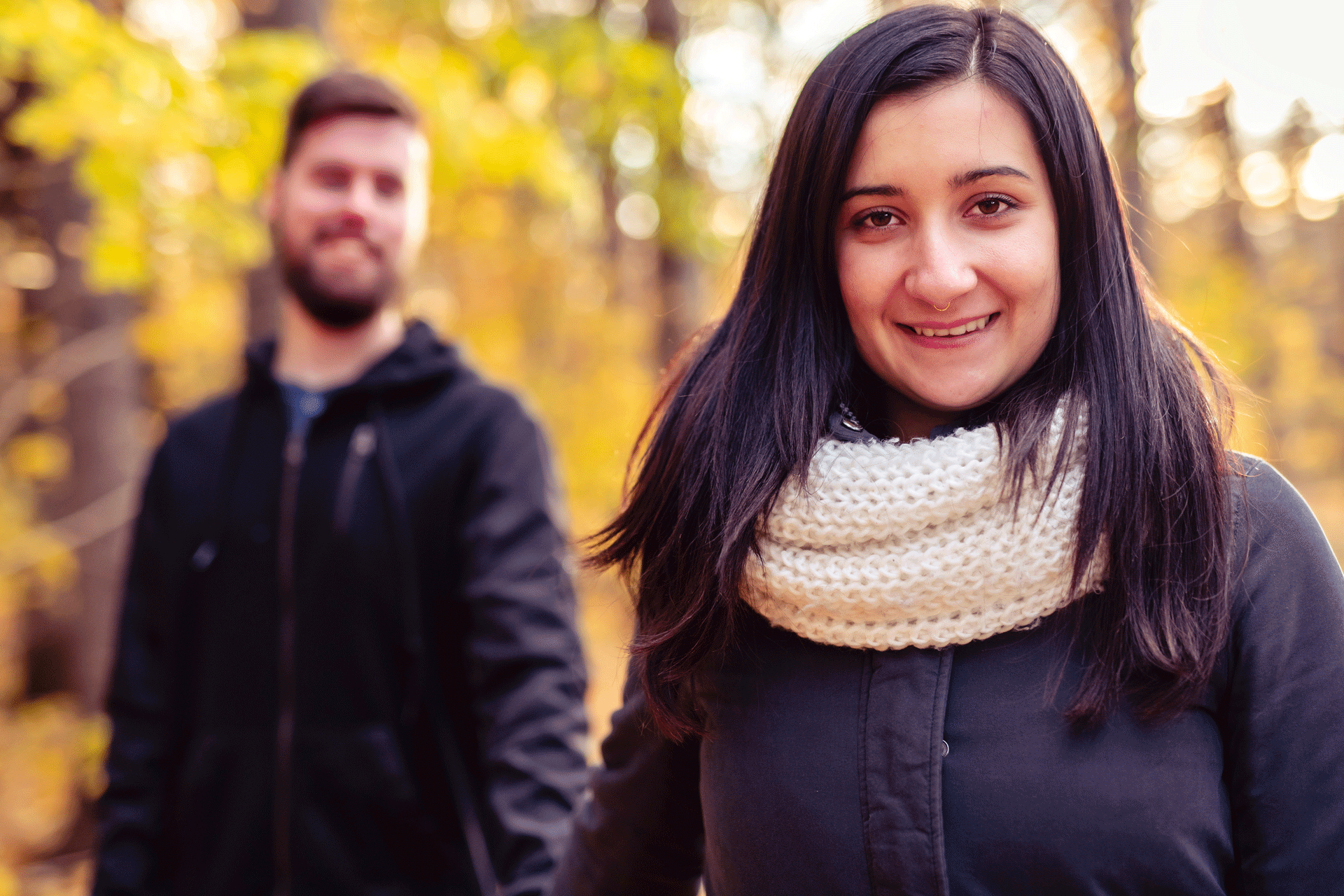 Happy Woman In Focus With Man In Background, Autumn Setting Conveying A Peaceful Walk For Anxiety Management happy woman in focus with man in background, autumn setting conveying a peaceful walk for anxiety management