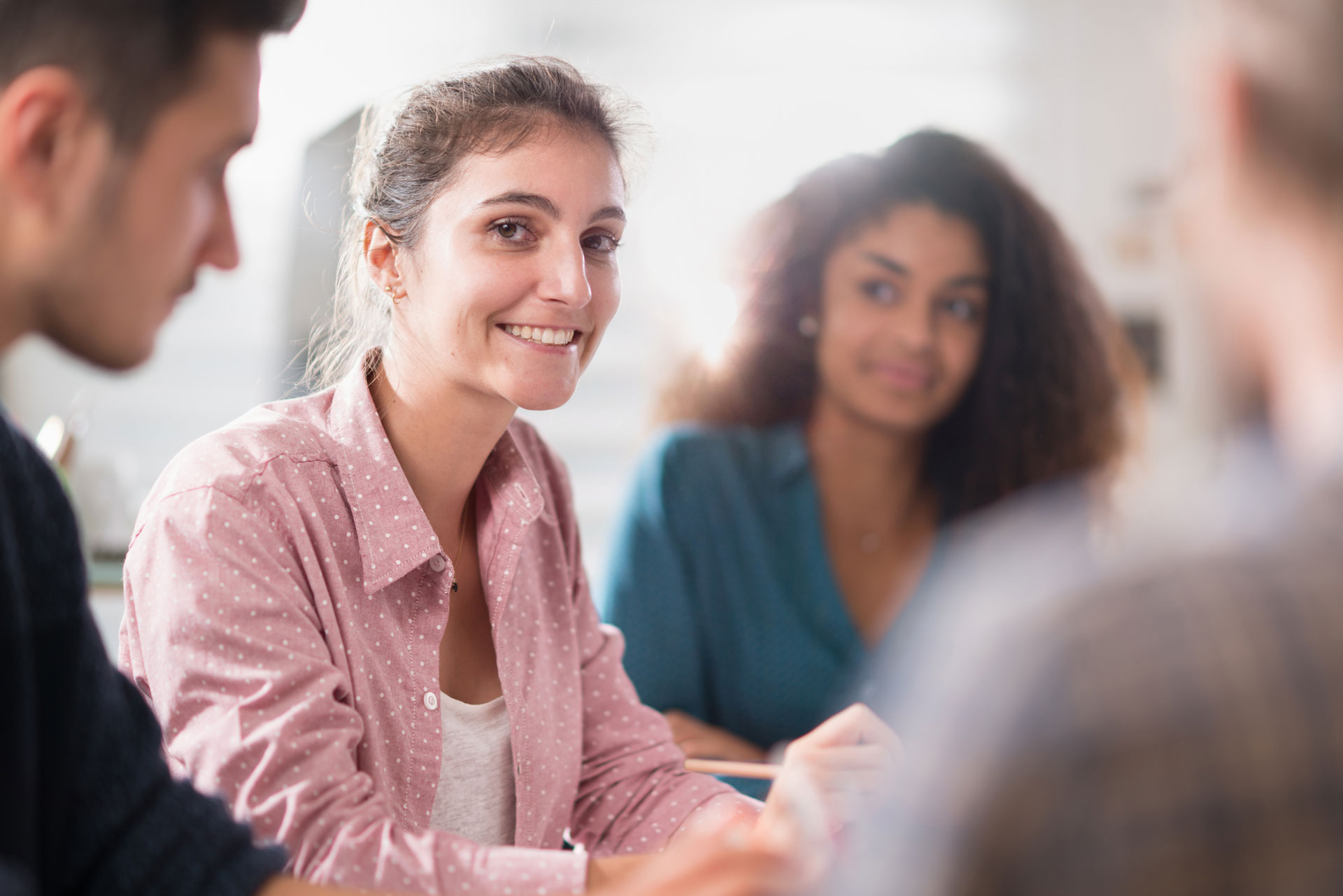 Group of people in a meeting with a focus on one smiling woman, possibly in a support group setting