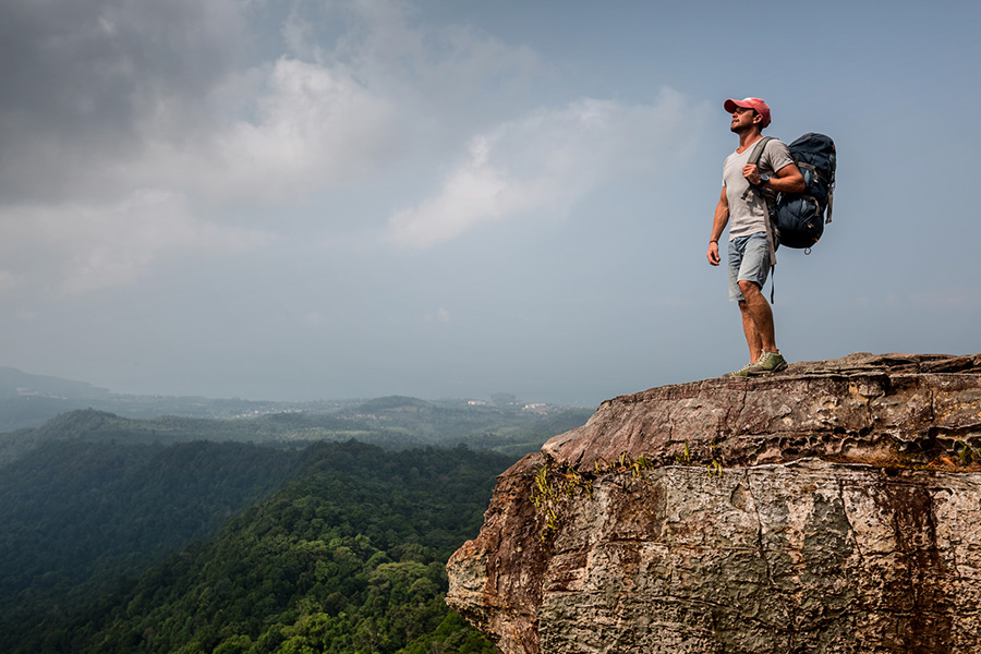 a hiker stands on a high cliff overlooking a vast mountain range, symbolizing peace and gratitude in recovery.