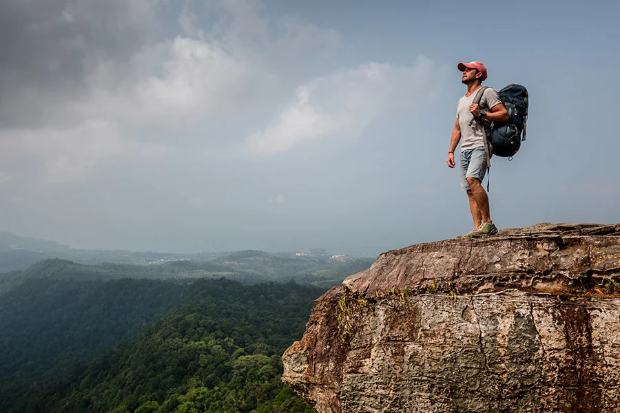 a hiker stands on a high cliff overlooking a vast mountain range, symbolizing peace and gratitude in recovery.