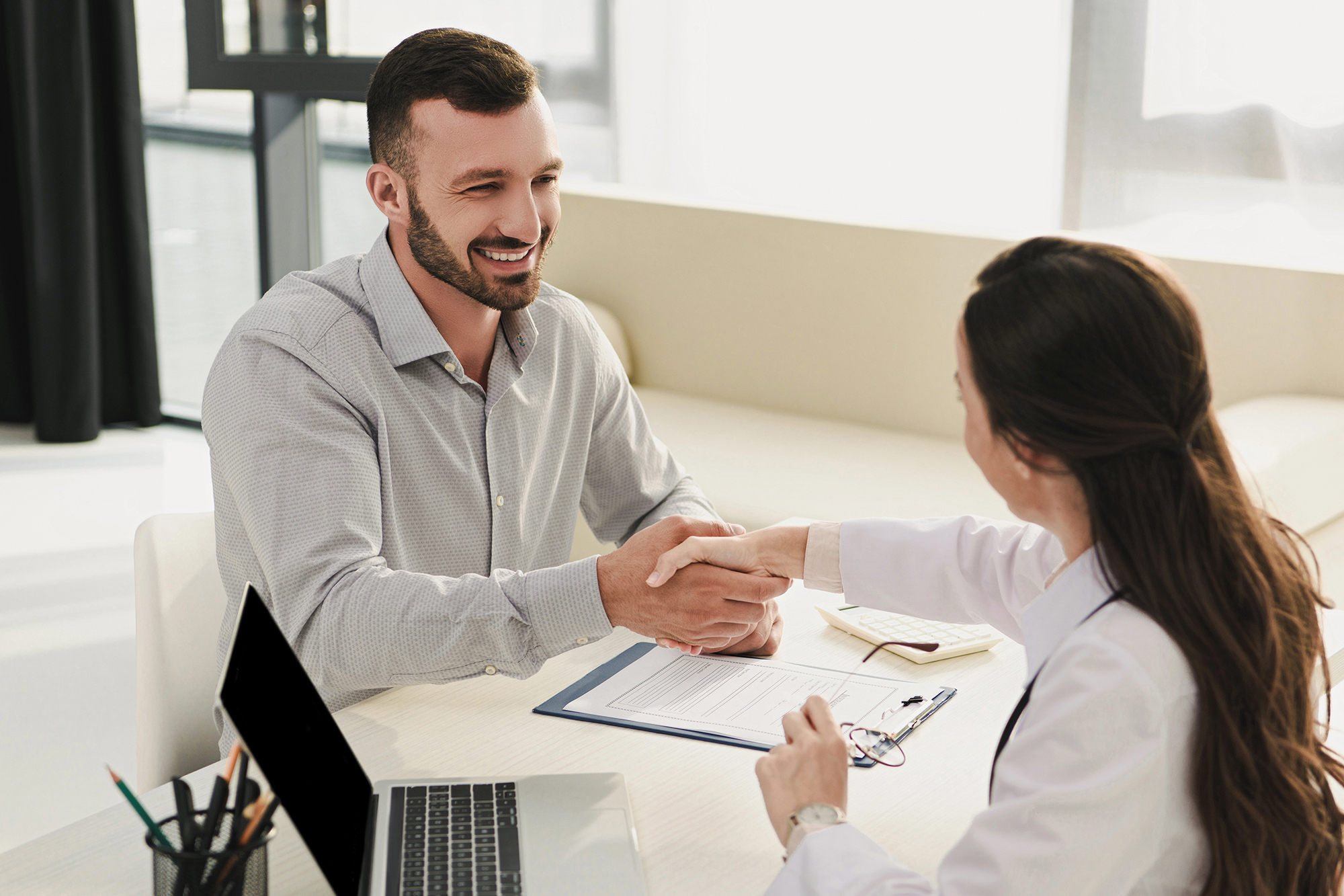 A man smiling and shaking hands with an admissions counselor in an office setting, highlighting the supportive admissions process