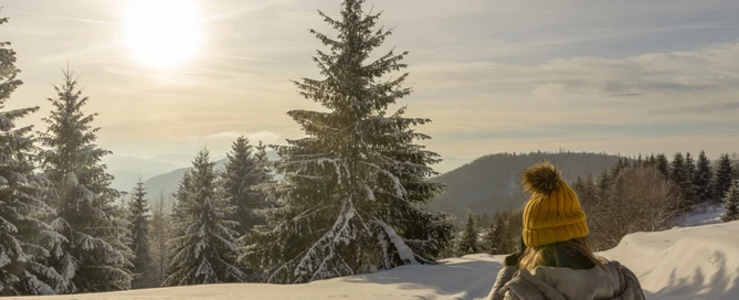 a woman in a yellow hat views a snowy forest, a calm scene for winter self-care for addiction recovery.