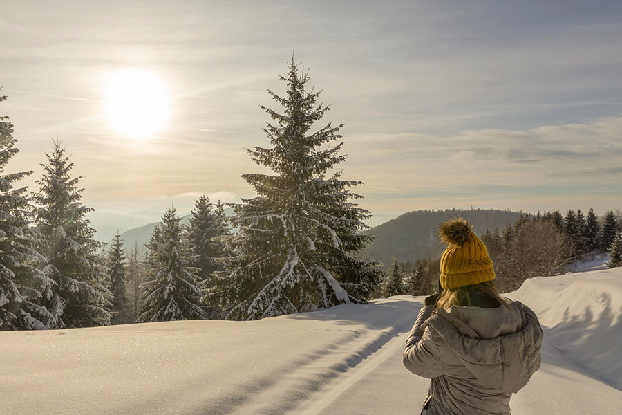 a woman in a yellow hat views a snowy forest, a calm scene for winter self-care for addiction recovery.