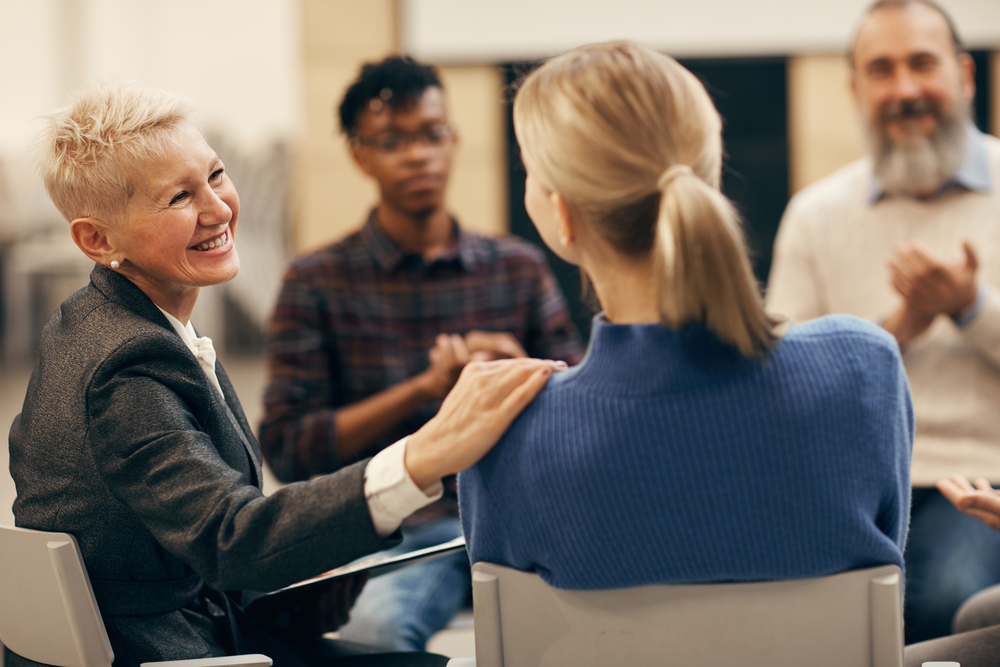 Group therapy session for co-occurring disorders, with a smiling therapist engaged in discussion with participants Group therapy session for co-occurring disorders, with a smiling therapist engaged in discussion with participants