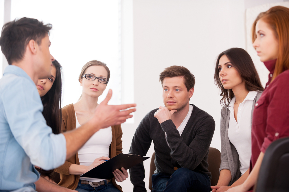 Group Of People Sitting Close To Each Other While Man Telling Something And Gesturing Group session led by mental health professionals, focusing on interactive