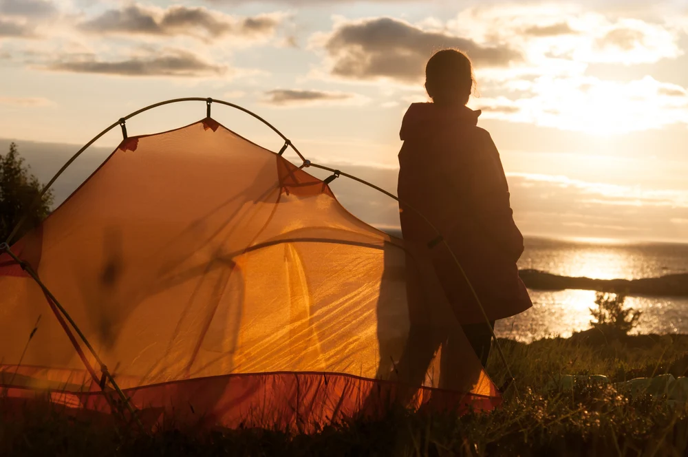 person by a tent at sunrise reflecting during a trauma counseling retreat