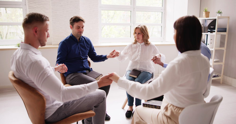 Group Of People Sitting Together Praying Group of people engaging in a nurturing group therapy atmosphere