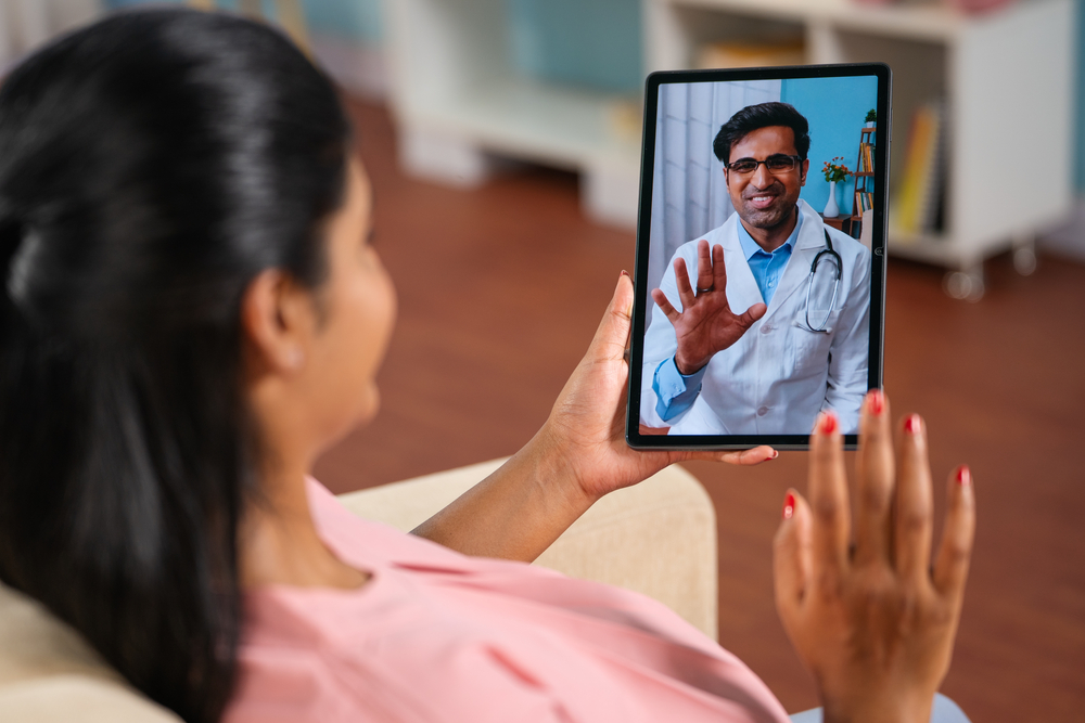 woman having a video call consult with a smiling male doctor on a tablet.