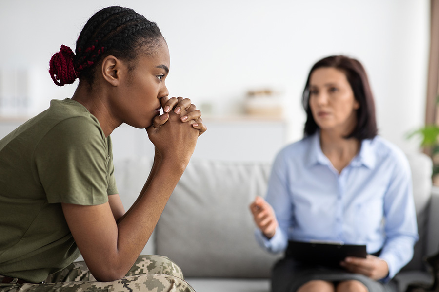 Female military receiving addiction treatment for veterans during a counseling session with a therapist on a sofa.