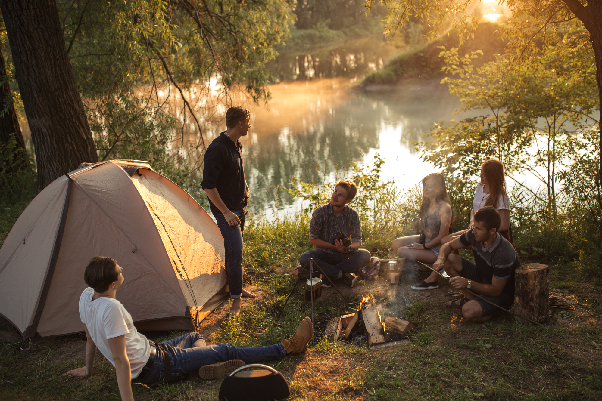 Group of people enjoying a camping trip by a lake, illustrating experiential therapy in a natural setting.