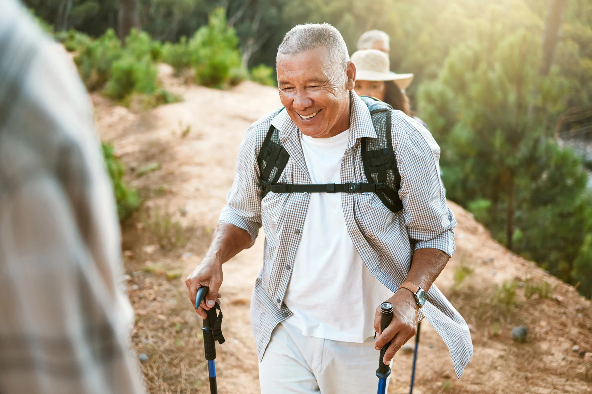 an older man smiles while hiking with a group on a mountain trail, representing the active life possible through addiction treatment and dual diagnosis care.