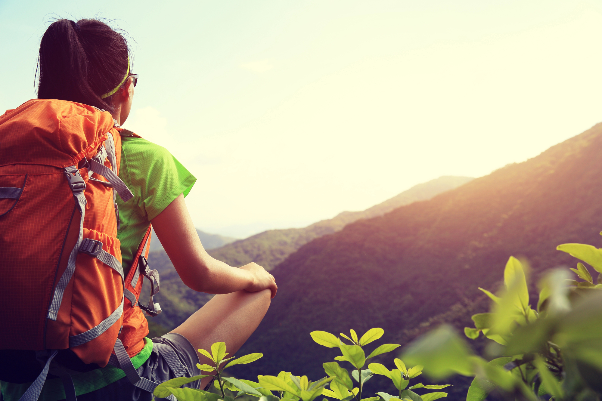 Person with an orange backpack sitting on a mountain trail at sunrise, symbolizing experiential therapy and PacificSource addiction coverage.