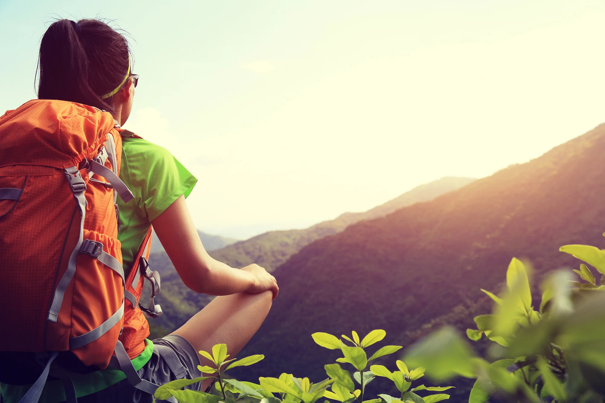 person with an orange backpack sitting on a mountain trail at sunrise, symbolizing experiential therapy and pacificsource addiction coverage.