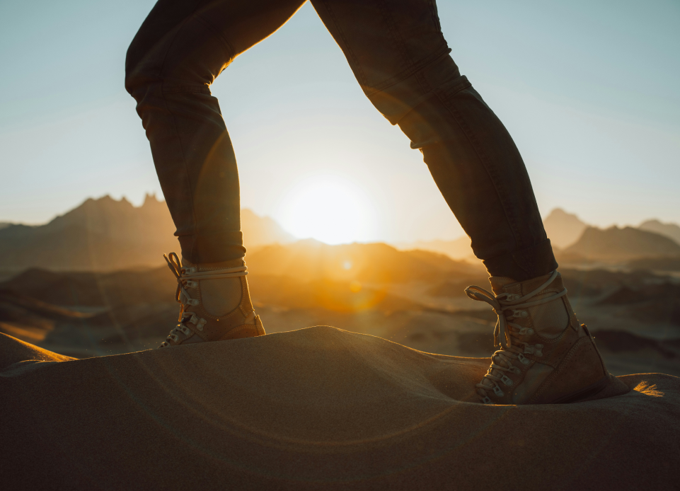  Hiker's legs standing on a dune at sunrise, symbolizing a journey in mental health recovery.