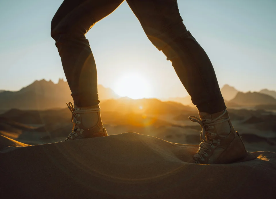 Hiker’S Legs Standing On A Dune At Sunrise, Symbolizing A Journey In Mental Health Recovery. hiker's legs standing on a dune at sunrise, symbolizing a journey in mental health recovery.
