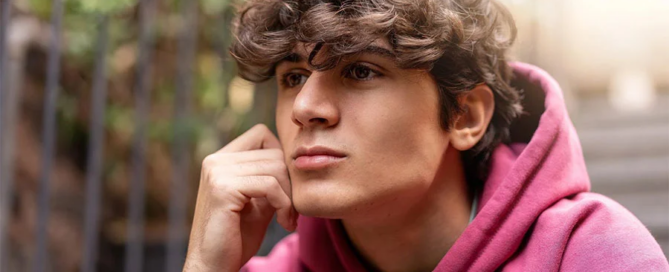 teen sitting outdoors with a thoughtful expression, reflecting on stress and emotions linked to teens cutting themselves