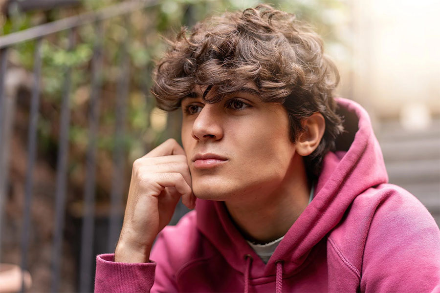 teen sitting outdoors with a thoughtful expression, reflecting on stress and emotions linked to teens cutting themselves