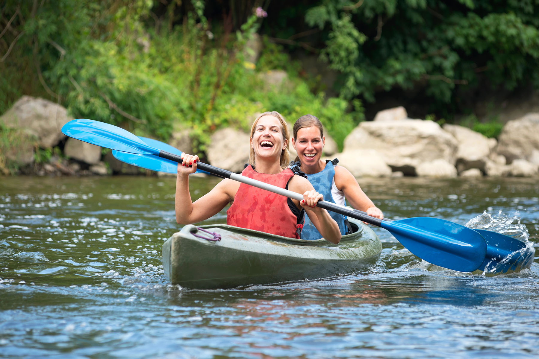 Two women kayaking on a river, smiling and enjoying outdoor activity, illustrating experiential therapy for addiction Two women kayaking on a river, smiling and enjoying outdoor activity, illustrating experiential therapy for addiction.
