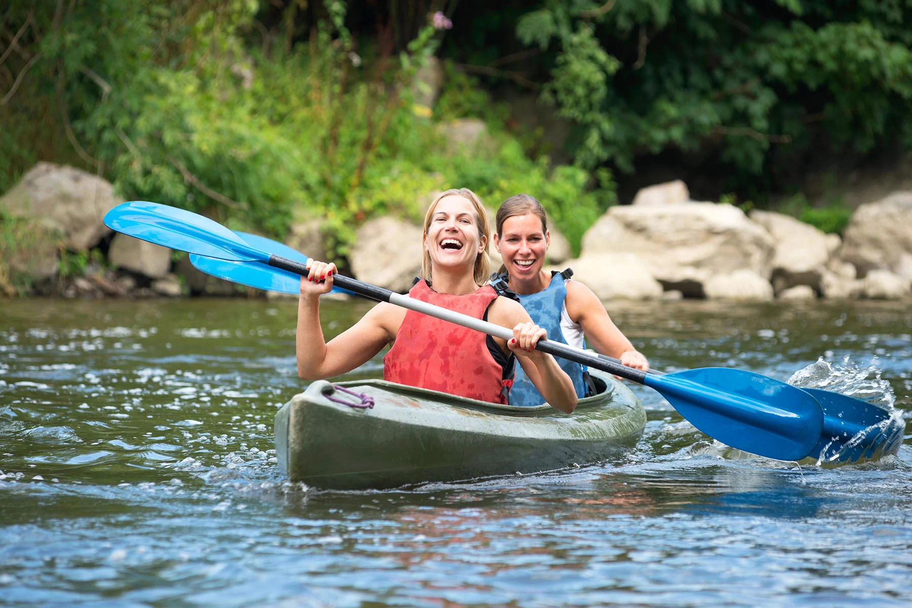 two women kayaking on a river, smiling and enjoying outdoor activity, illustrating experiential therapy for addiction.
