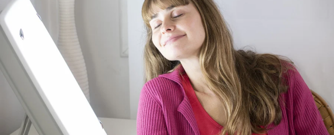 woman sitting near a white light lamp for light therapy to treat sad.