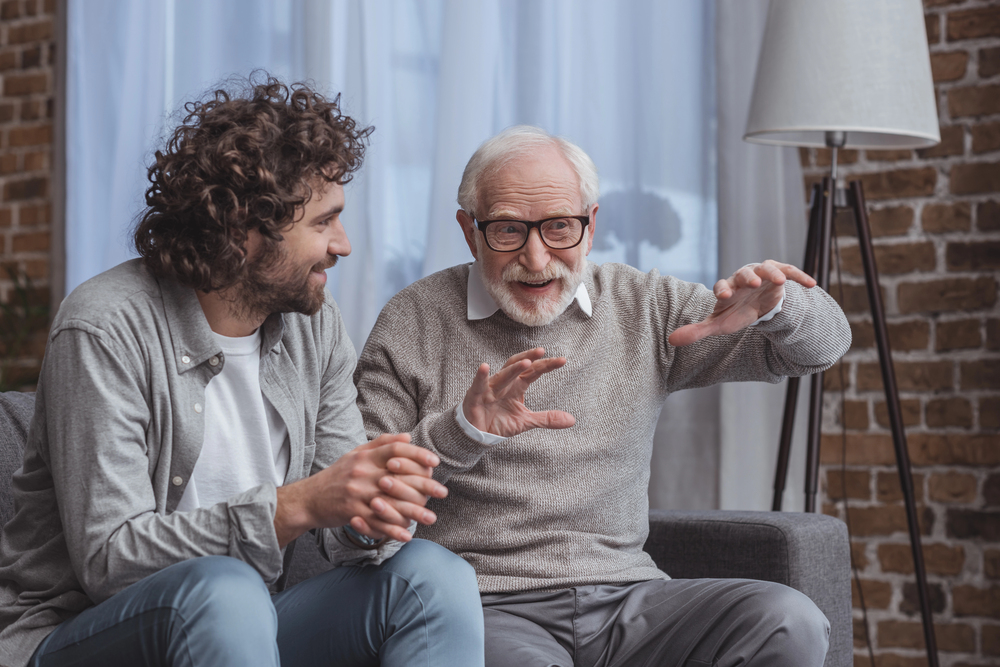 Adult son and senior father talking about addiction treatment on sofa at home.