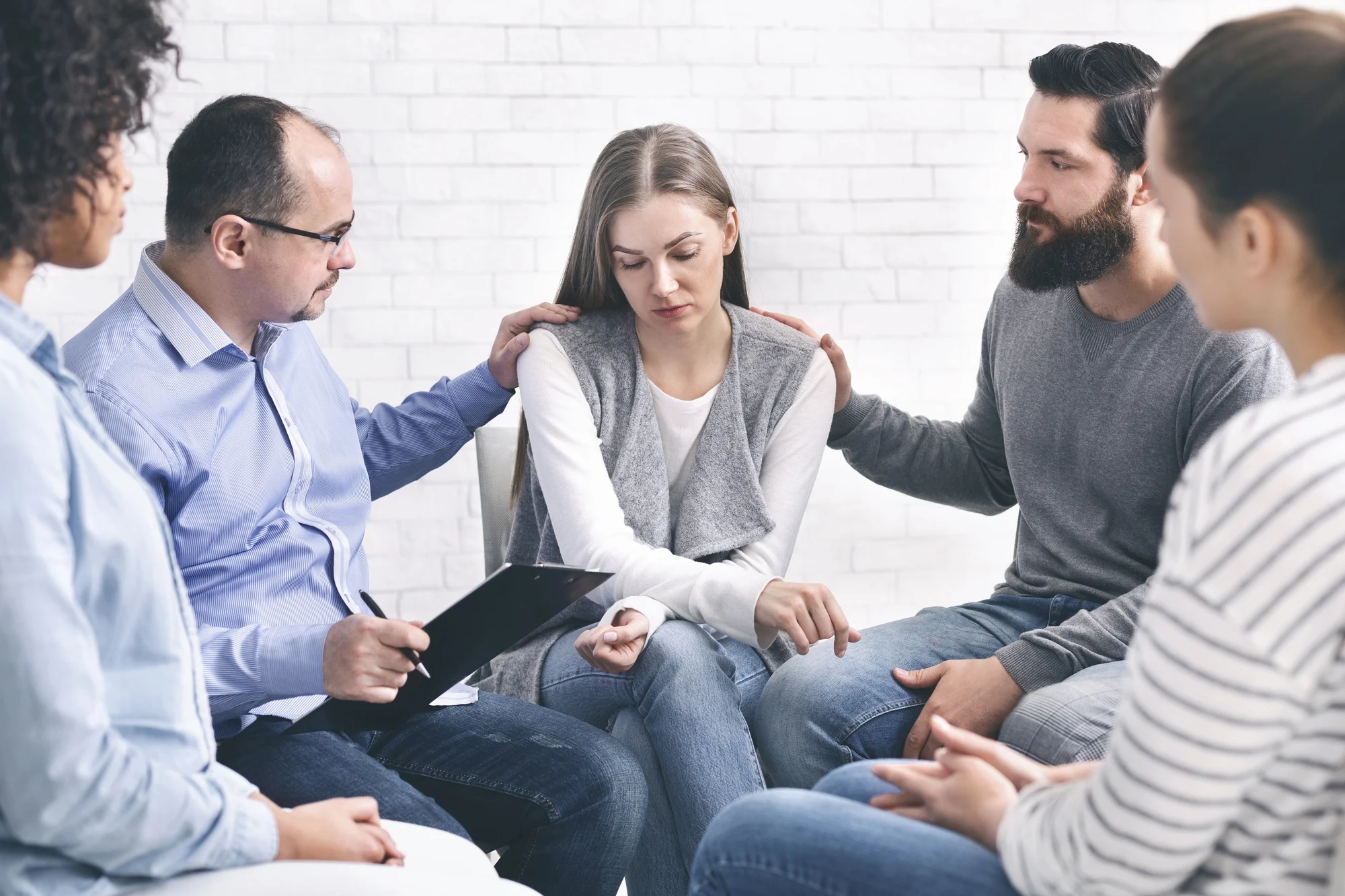 a support group sitting in a circle, offering comfort to a young woman, illustrating the benefits of addiction coverage and dual diagnosis care.