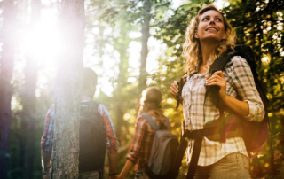 a smiling woman hikes through a sun-drenched forest, representing the journey toward wellness with bcbsmt addiction coverage and dual diagnosis support.