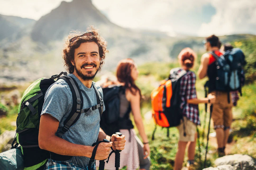 A Smiling Man Hiking With A Group In The Mountains, Illustrating The Healthy Lifestyle Supported By Bcbs Of Montana Dual Diagnosis Coverage. a smiling man hiking with a group in the mountains, illustrating the healthy lifestyle supported by bcbs of montana dual diagnosis coverage.